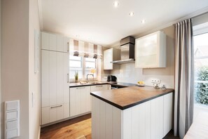 A modern kitchen with white cabinets, a wooden countertop, and a built-in stove. - House Steinmannstraße 77, half of the house A (Sylt)