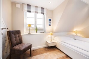 A bedroom with a bed, bedside tables, a chair, a window with curtains, and a radiator. - House at Steinmannstraße 77, half of House A (Sylt)