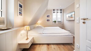 A modern bedroom with a bed, bedside tables, a window with curtains, and a wall-mounted TV. - House Steinmannstraße 77, half of the house A (Sylt)
