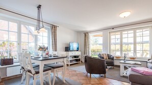 Un salon spacieux comprenant un coin repas, de grandes fenêtres et un téléviseur.