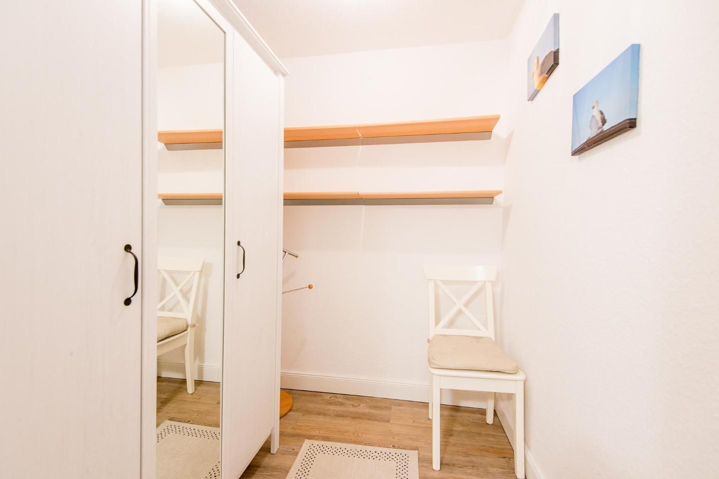 Una habitación con un armario blanco, una silla blanca, suelo de madera y una alfombra pequeña.