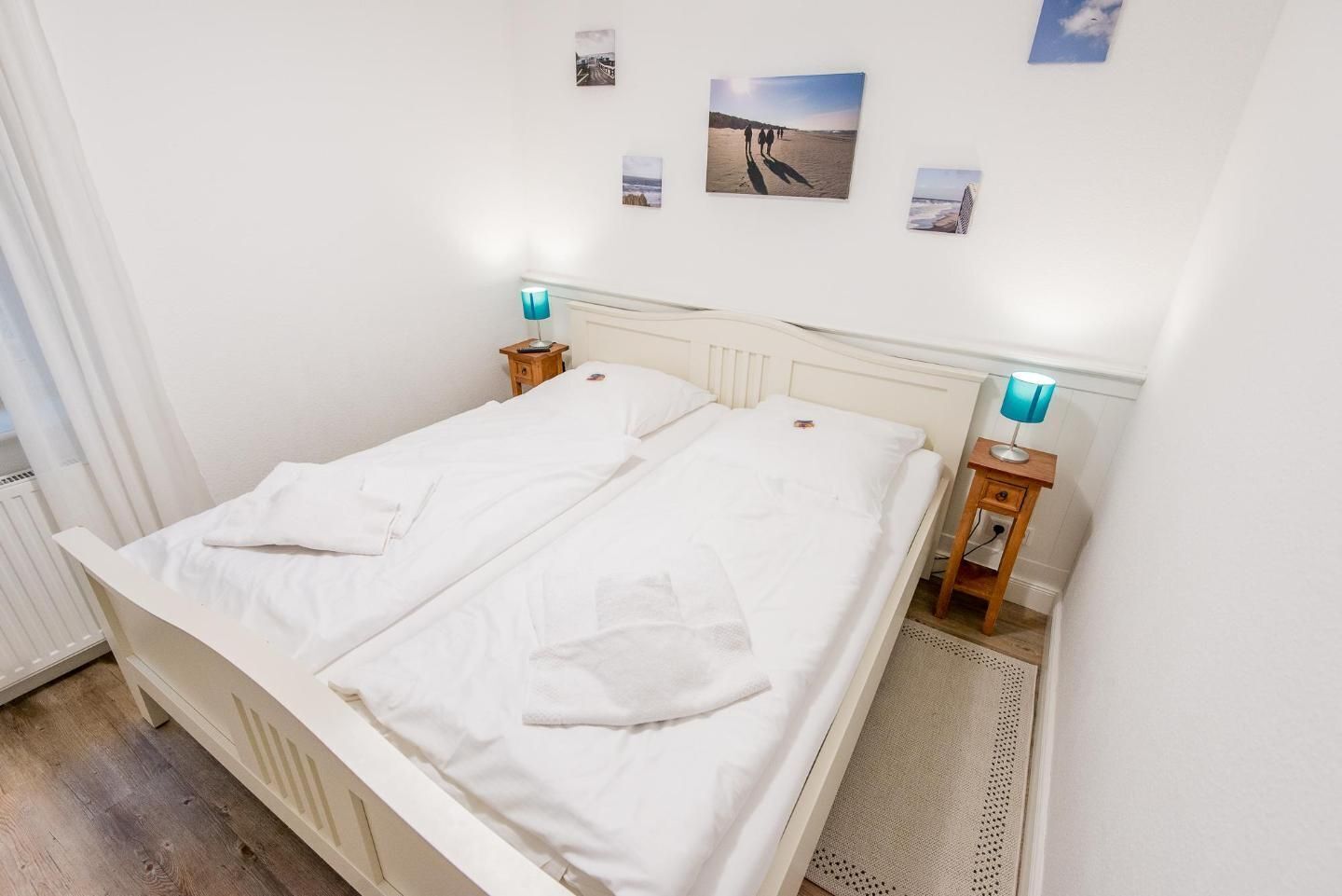 A double bed with white linens, two bedside tables with lamps, and a small rug.