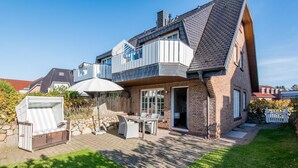 Une maison à deux étages dotée d’un patio aménagé avec des meubles d’extérieur et un espace salon couvert.