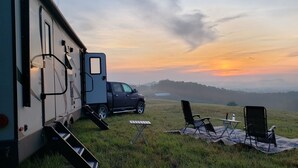 Una caravana estacionada en un camp verd amb un cel capvespre al fons.