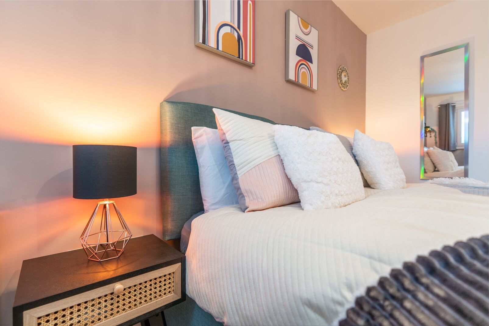 Une chambre d’hôtel bien rangée, avec un lit, une lampe de chevet et des œuvres d’art accrochées au mur.