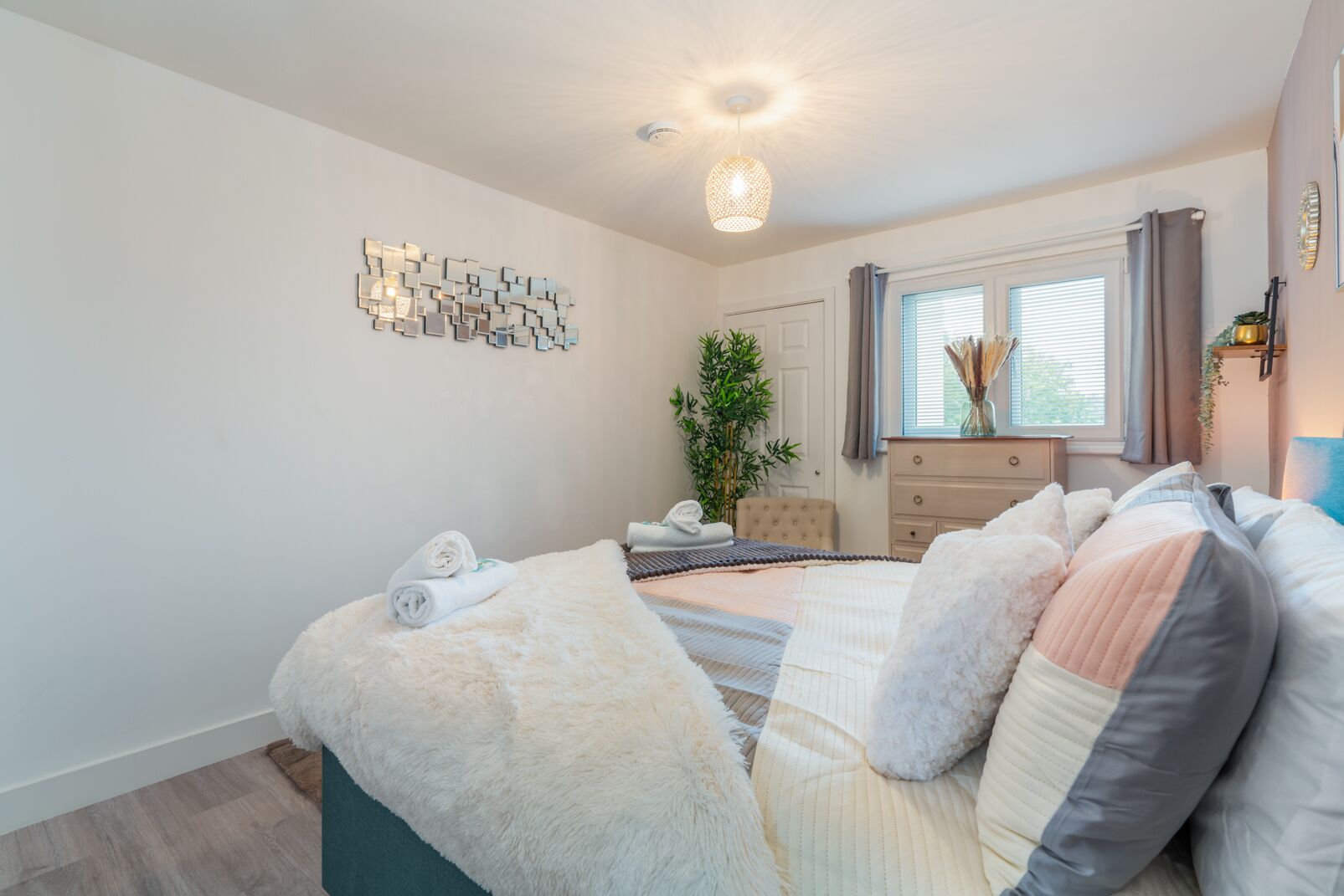 A modern bedroom with a large bed, a dresser, a mirror, and a wall art piece.