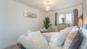 A modern bedroom with a large bed, a dresser, a mirror, and a wall art piece.