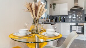 A modern kitchen with a glass dining table, white chairs, and a vase with pampas grass.
