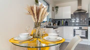 A modern kitchen with a glass dining table, white chairs, and a vase with pampas grass.