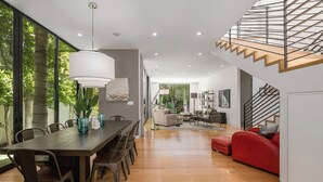 Un vaste espace de vie comprenant une table à manger en bois, un canapé rouge et un escalier doté d’une rampe en verre.