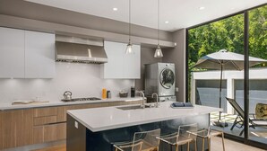 Une cuisine moderne dotée d’un grand îlot central, de tabourets de bar et offrant une vue sur l’extérieur grâce à de grandes fenêtres.
