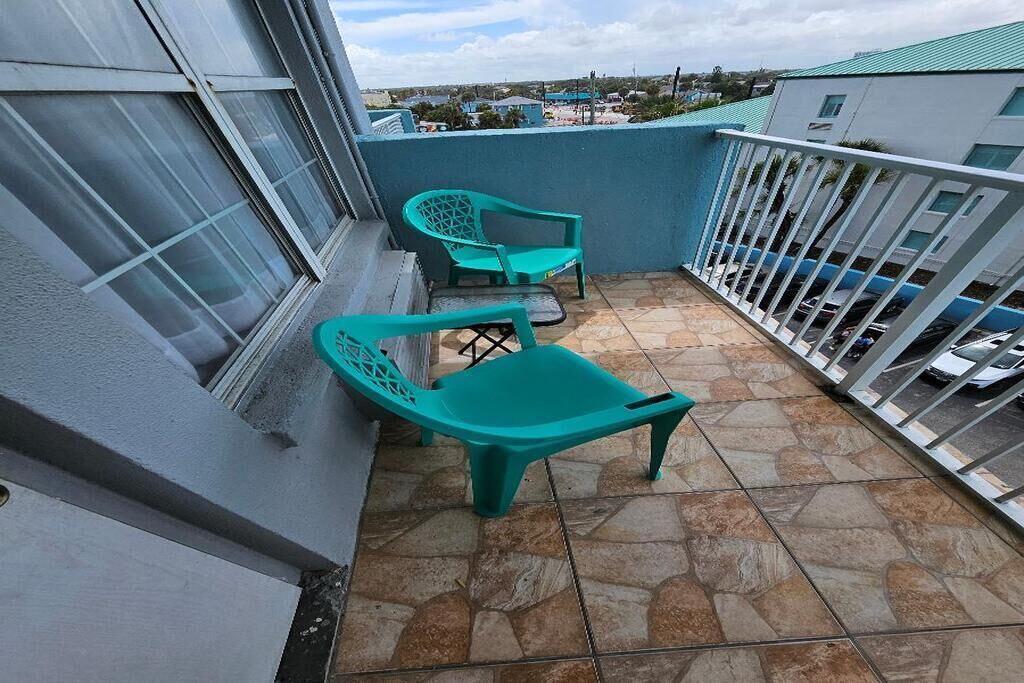 A balcony with two turquoise plastic chairs, a tiled floor, and a view of the surrounding area.
