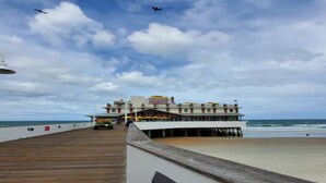 A pier leading to a multi-story building with a beach view. - OCEAN VIEW SUITE WITH FULL KITCHEN (Daytona Beach)