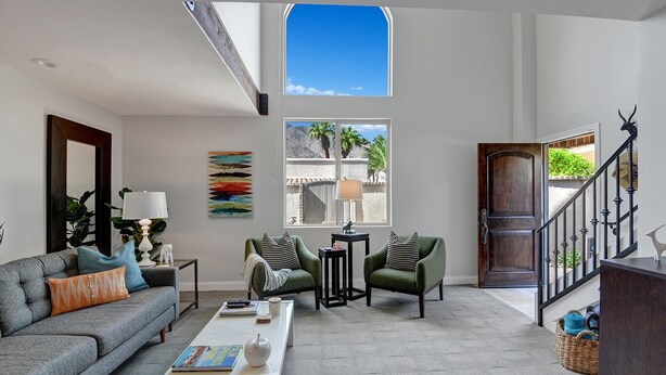 Amplia sala de estar con techo alto, ventana grande, una escalera y puerta que da a un espacio exterior.