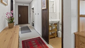 En hall med ett träbord, en röd matta, en dörr och ett badrum med handfat och spegel.