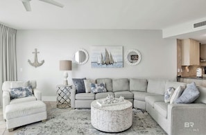 A living room with a grey sectional sofa, a round coffee table, and a painting of sailboats.