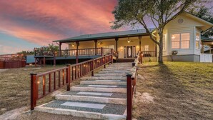 A two-story house with a covered porch and a staircase leading to the entrance. - Gated 10-Acre Compound | Sleeps 28 | Game Room (Spicewood)