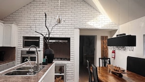 Cuina moderna amb un lucernari, parets de maó blanc i zona de menjador amb taula i cadires de fusta.