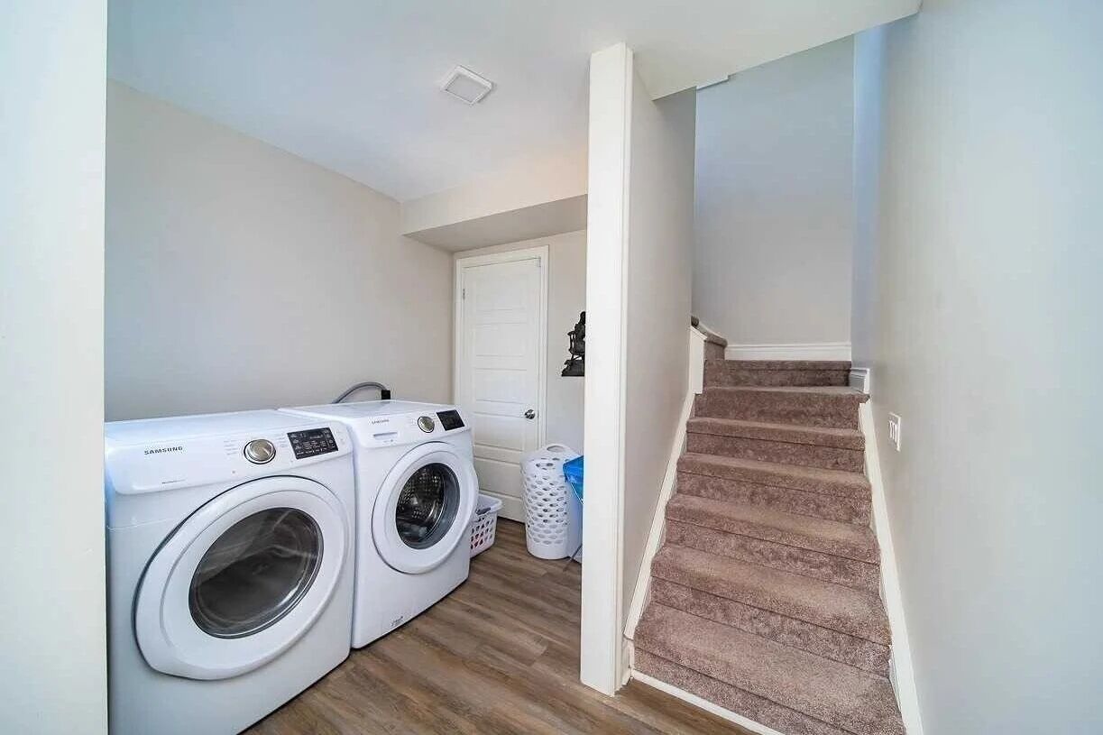 A laundry area with two white washing machines, a white door, and a carpeted staircase.