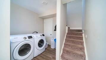 A laundry area with two white washing machines, a white door, and a carpeted staircase.