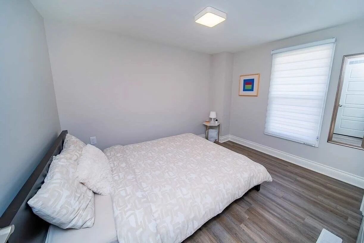 A bedroom with a bed, a nightstand, a lamp, and a window with blinds.