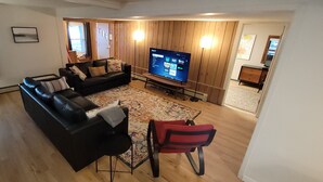 A living room with a black sofa, a red chair, a TV, and a wooden floor.
