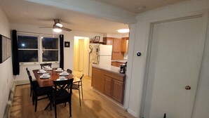 A dining area with a wooden table set for four, a ceiling fan, and wooden cabinets in the adjacent kitchen.