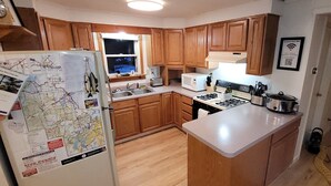 A kitchen with wooden cabinets, a refrigerator with maps, a stove, and a sink.