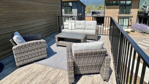 A deck with wicker furniture and a view of modern buildings. - 40 Mins to Glacier Park, 5 Mins to City Beach & DT (Whitefish)