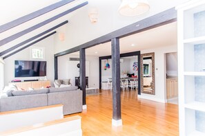 Uma sala de estar espaçosa com design moderno, apresentando um sofá cinza grande, piso de madeira e uma televisão sobre um móvel de madeira.