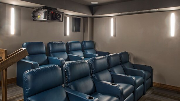 Sala de cine en casa con sillones reclinables de cuero azul, una escalera de madera y un proyector instalado en el techo.