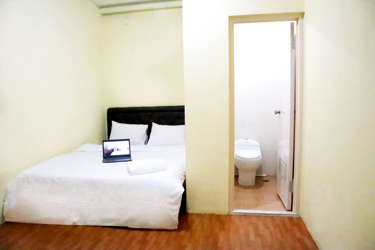 A small, clean room with a bed, a bedside table, and a door leading to a bathroom.