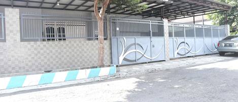 A gated property with a covered parking area, a tree, and a car parked inside.