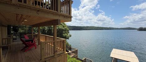 A wooden deck with a view of a lake, a dock, and a small boat.