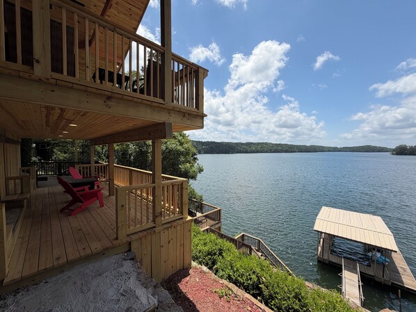 A wooden deck with a view of a lake, a dock, and a small boat.