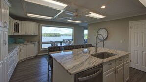 Cucina con mobili bianchi, piano di lavoro in marmo, lavello incassato e vista su un lago.
