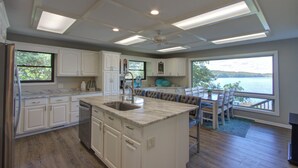 Una cucina moderna con mobili bianchi, una grande isola con lavello e vista sul lago tramite ampie finestre.