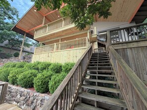 A wooden staircase leading to a balcony with a view of a stone wall and green bushes.
