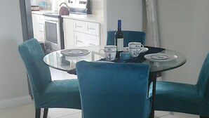 A dining area with a round glass table, teal upholstered chairs, and a white cabinet in the background. - Tastefully decorated nautical Oasis in the Richmond Estate subdivision awaits yo (St. Ann Parish)