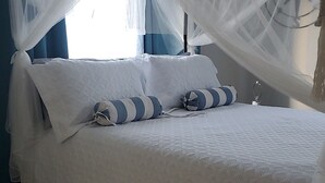 A bed with a white canopy, two pillows, and a bedside table with a glass object. - Tastefully decorated nautical Oasis in the Richmond Estate subdivision awaits yo (St. Ann Parish)