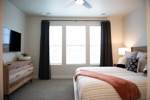 A hotel room with a bed, a dresser, a TV, and a window with curtains.