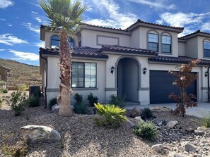 A two-story house with a tiled roof, a garage, and a landscaped front yard with rocks and plants.