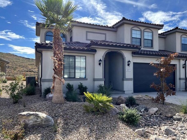 A two-story house with a tiled roof, a garage, and a landscaped front yard with rocks and plants.