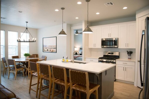 A modern kitchen with white cabinets, a central island with bar stools, a microwave, stove, and refrigerator.