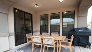 Patio esterno con tavolo e sedie in legno, un barbecue e ampie finestre.