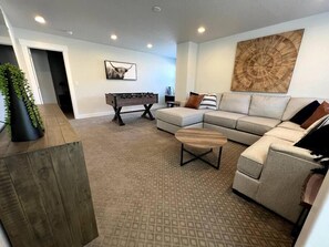 A modern living room with a sectional sofa, a foosball table, and a large wall art piece.