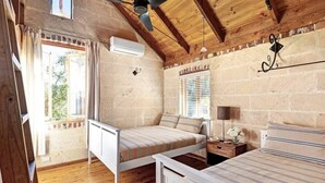 Een slaapkamer met een houten plafond, een bed met gestreepte lakens, een nachtkastje met een lamp en een raam met zonwering.