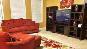 A living room with a red sectional sofa, a flat-screen TV, and a floral rug.
