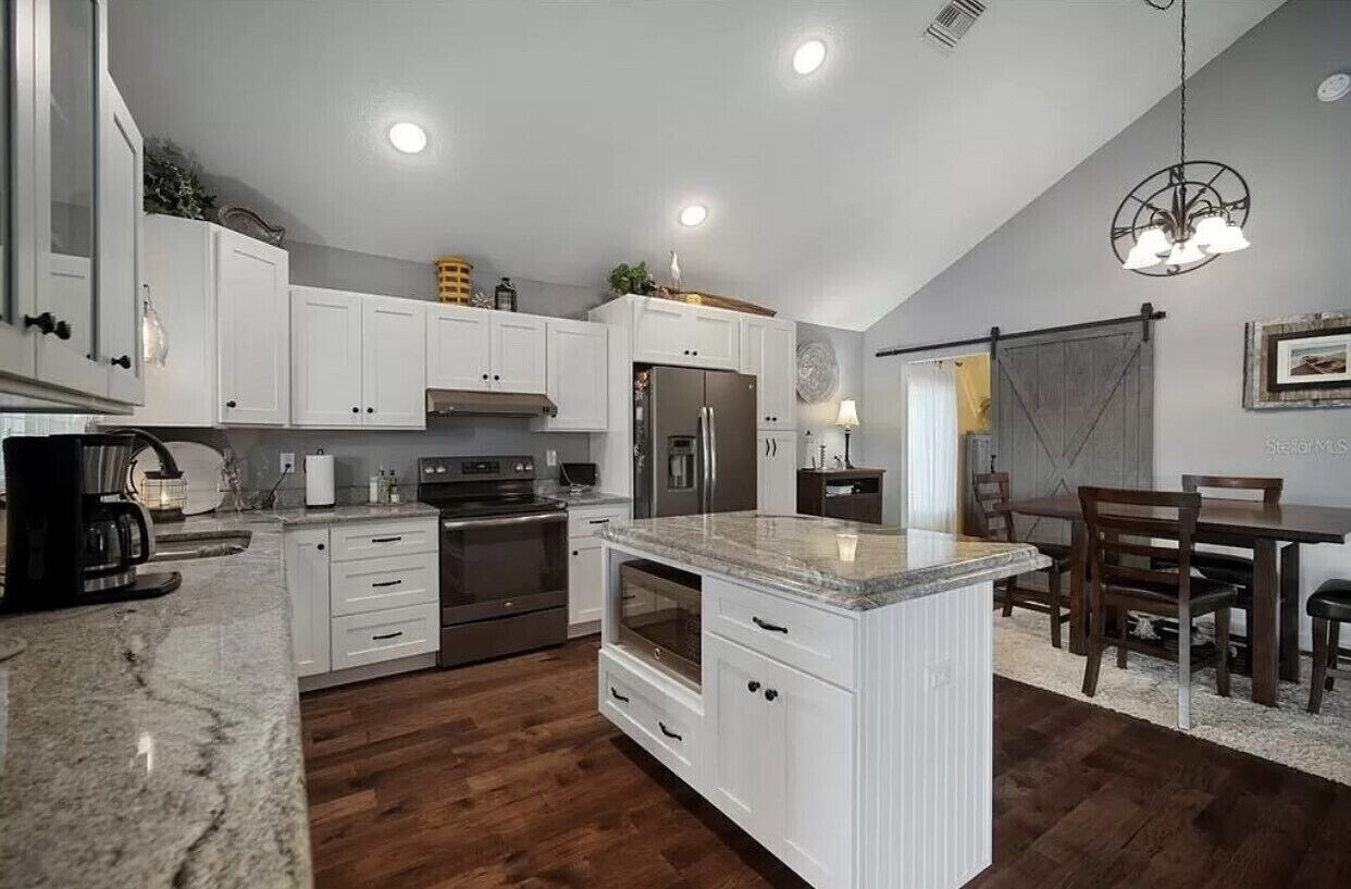 A modern kitchen with white cabinetry, a granite countertop, stainless steel appliances, and a dining area with wooden furniture.