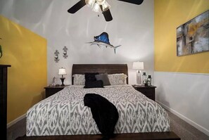 A bedroom with a bed, nightstands, a ceiling fan, a wall-mounted artwork, and a decorative fish decal.